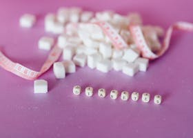 Sugar Cubes Beside Tape Measure Near Dices with Letter on a Pink Surface